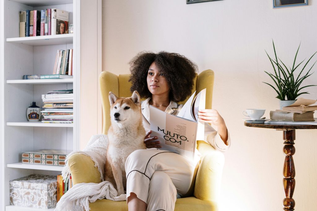 Woman reading a magazine at home with her Shiba Inu dog on a cozy chair.