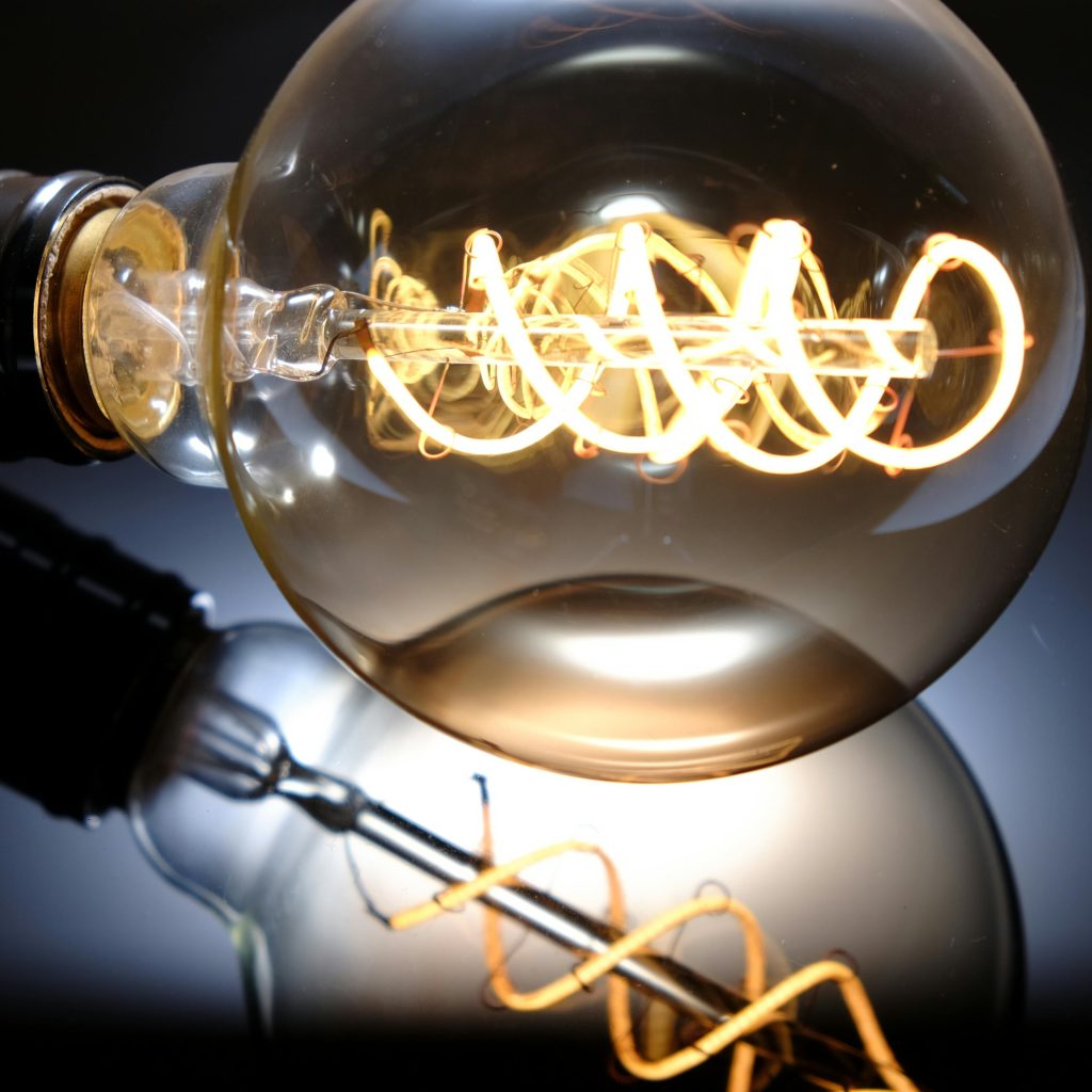 Close-up of a glowing vintage Edison light bulb with intricate filament pattern and reflection.
